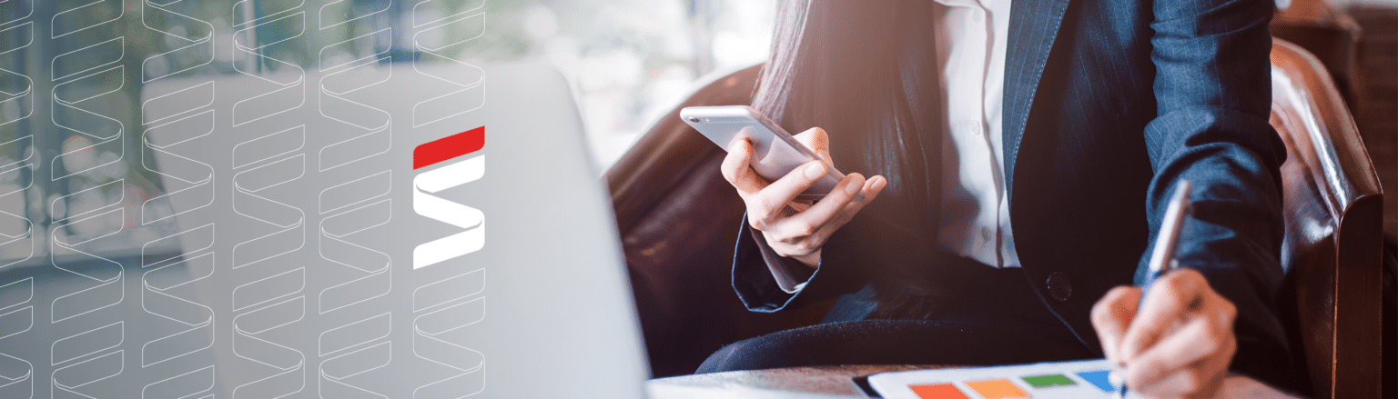 Close up photo of woman looking at phone while working on paperwork in front of a computer. Fraser Stryker logo icon repeating on the left side of the photo.