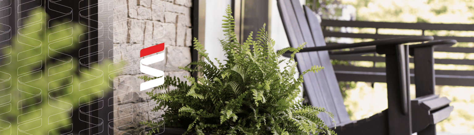 A cozy porch scene featuring a potted fern in the foreground, a stone wall to the side, and a wooden rocking chair overlooking a bright outdoor area with a blurred background of trees and a railing. Fraser Stryker logo icon repeating on the left side of the photo.