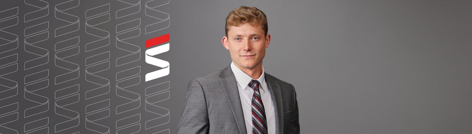 Photo of Kade Moural, wearing a white shirt, a stripped tie, and a grey suit. Fraser Stryker logo icon repeating on the left side of the photo.