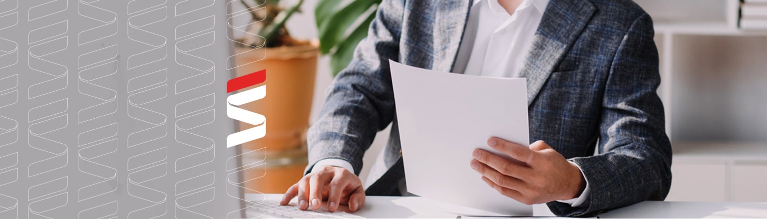 Photo of person looking at a piece of paper in front of a computer monitor. Fraser Stryker logo icon repeating on the left side of the photo.