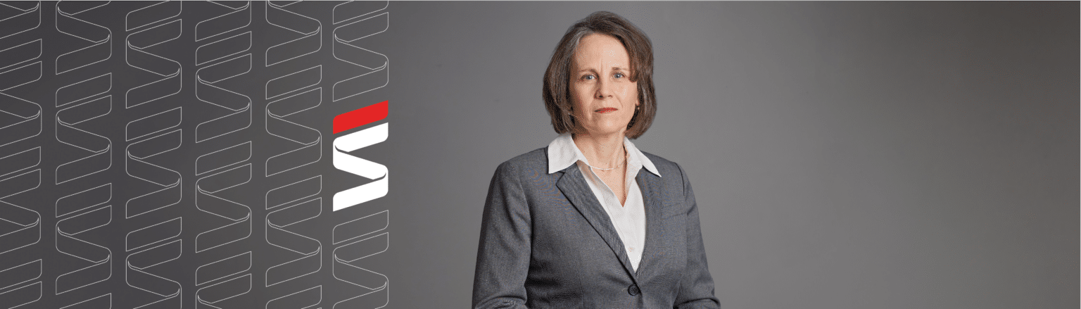 Mary Carnazzo, Fraser Stryker attorney, wearing a grey suit jacket, white shirt, and black pants. Fraser Stryker logo icon repeating on the left side of the photo.