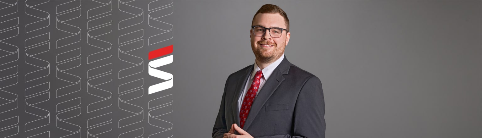Trevor Rogers, Fraser Stryker attorney, wearing a dark grey suit, white shirt and red tie. Fraser Stryker logo icon repeating on the left side of the photo.