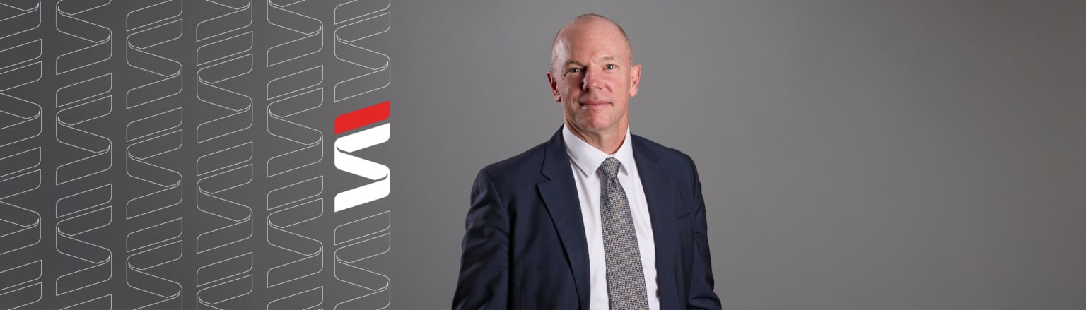 John McCarthy, Fraser Stryker attorney, wearing a dark blue suit, white shirt button down shirt, and blue patterned tie. Fraser Stryker logo pattern on the left side.