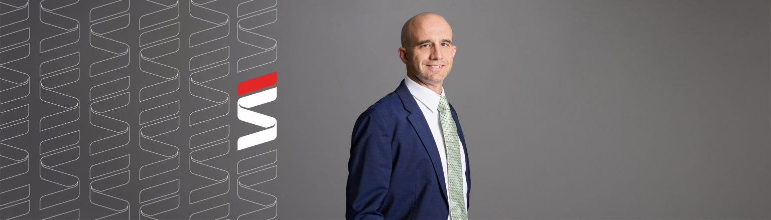 Dillon Shea, Fraser Stryker attorney, wearing a dark blue jacket, white shirt button down shirt, and green and blue patterned tie. Fraser Stryker logo pattern on the left side.