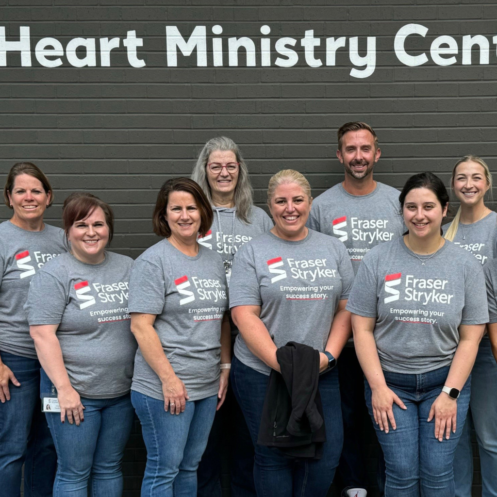 Group of people standing outside the Heart Ministry Center in Omaha, NE wearing Fraser Stryker logoed t-shirts with the statement "Empowering your success story."