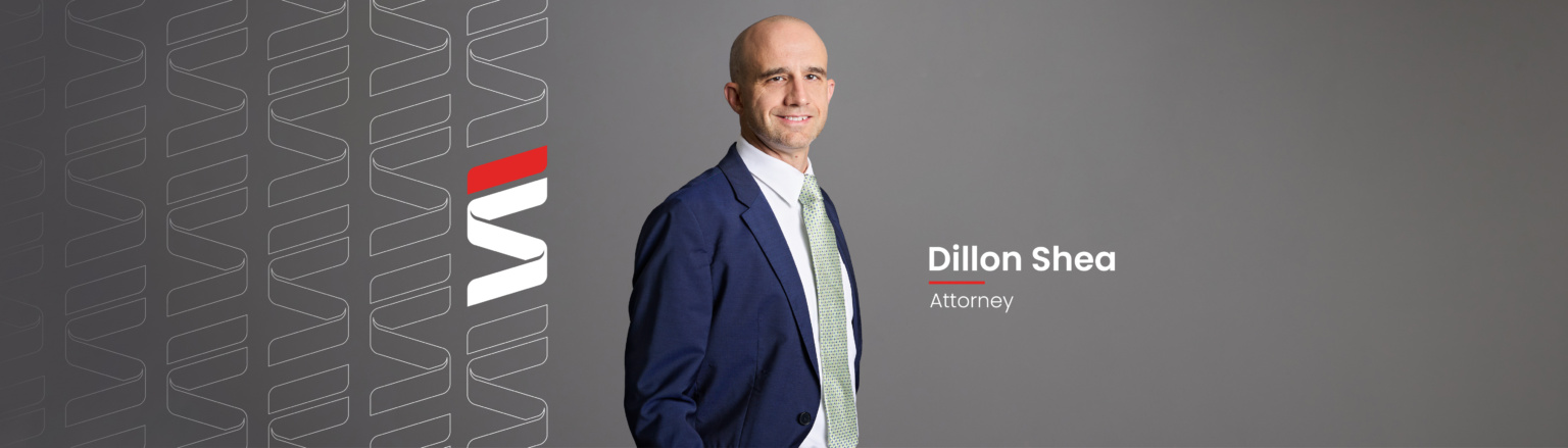 Dillon Shea, Fraser Stryker attorney, wearing a dark blue jacket, white shirt button down shirt, and green and blue patterned tie. Fraser Stryker logo pattern on the left side.