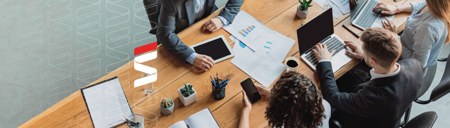 Close up aerial photo of people at a table with computers, paperwork and tablets, holding a business meeting. Fraser Stryker logo icon repeating on the left side of the photo.